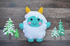 a crocheted stuffed animal with horns standing in front of some snow covered trees