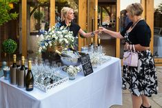 two women standing at a table with wine glasses and bottles