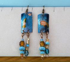 "These eclectic earrings are handmade from 1.25\" copper that has been enameled in shimmering blue, green, and amber tones. Unique turquoise and amber glass beads dangle below. They hang on French wire hooks." Blue Artisan Copper Earrings, Artisan Blue Copper Earrings, Unique Blue Copper Earrings, Artsy Blue Beaded Dangle Earrings, Blue Artsy Beaded Dangle Earrings, Bohemian Blue Copper Earrings, Artsy Blue Beaded Earrings, Bohemian Blue Earrings, Eclectic Earrings