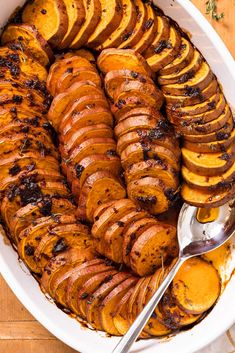 cooked sweet potatoes in a white dish with a serving spoon and herbs on the side