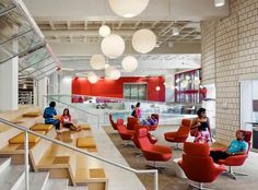 people are sitting on red chairs in an open area with stairs and glass railings