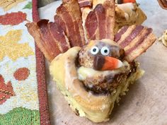 a turkey shaped pastry with bacon on it's side and another food item in the background