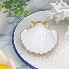 a shell shaped ring sitting on top of a white plate next to a flower pot