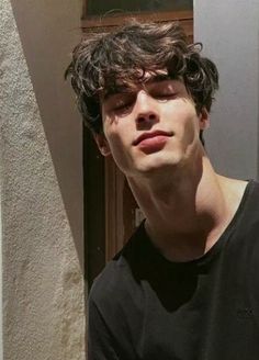 a young man with curly hair standing in front of a door and looking at the camera