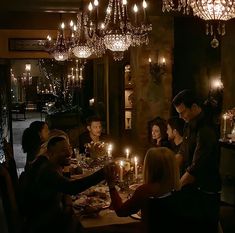 a group of people sitting around a dinner table with candles in the middle of it