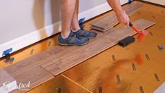 a man is using a hammer to cut through the wood flooring on top of a wooden plank