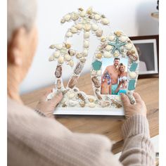 an elderly woman holding up a photo frame with shells on it