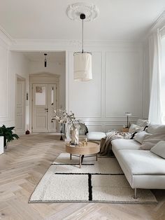 a living room with white furniture and wood flooring, along with a rug on the floor