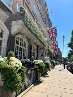 an english flag is hanging on the side of a brick building with white flowers in front