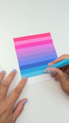 two hands holding a pen over a piece of paper with color swatches on it