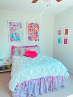 a bedroom with white walls, pink and blue bedding and pictures on the wall