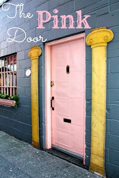 the pink door is painted on the side of this gray brick building with yellow columns