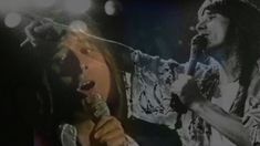 a woman singing into a microphone in front of an image of a man with long hair