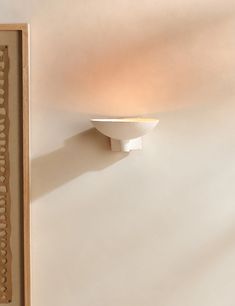 a white wall light mounted on the side of a wall next to a framed photograph