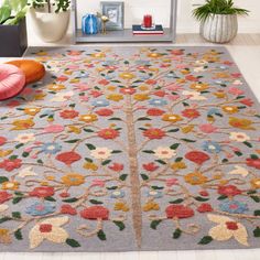 an area rug with flowers and leaves on the floor in front of a couch, potted plant