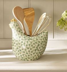 a green and white chicken shaped container with wooden spoons, spatulas and other kitchen utensils