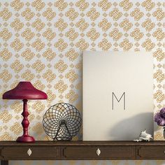 a table with a lamp, vase and other items on it in front of a wallpapered background