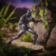 an action figure is posed on a rock in front of some plants and rocks,