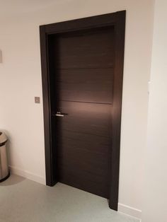 an empty room with a brown door and trash can on the floor next to it