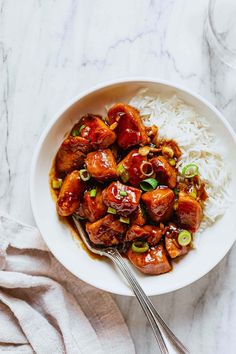 a white bowl filled with meat and rice next to a glass of water on a marble surface