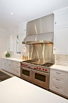 a large kitchen with white cabinets and stainless steel stove top oven in the middle of the room