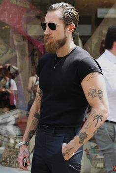 a man with tattoos on his arms and chest walking down the street while wearing sunglasses