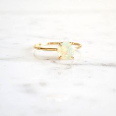 a white opal ring sitting on top of a marble counter with a gold band