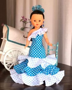 a doll in a blue and white dress next to a carriage