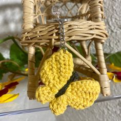 a crocheted butterfly keychain hanging from a wicker chair with flowers in the background