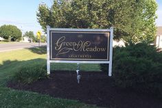 a sign for the green meadow apartments in front of some bushes and trees on a sunny day