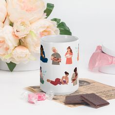 a coffee mug sitting on top of a table next to some chocolates and flowers