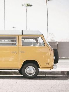 an old yellow van is parked on the side of the road with palm trees in the background