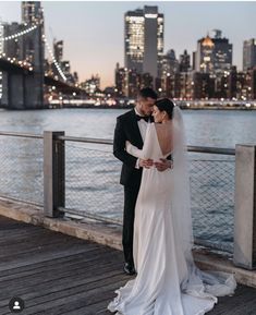 a bride and groom standing on a pier in front of the city skyline at night