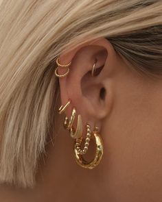 a woman with blonde hair wearing gold ear cuffs and hoop earrings in front of her face