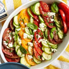 a white bowl filled with cucumbers, tomatoes and feta cheese on top of a yellow towel