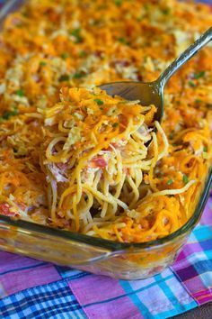 a glass casserole dish filled with pasta and cheese, topped with a serving spoon