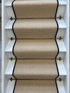 a carpeted stair case with black trim on the top and bottom, in front of a white wall