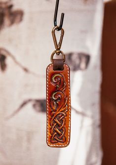 a leather keychain hanging from a hook with an intricate design on the front