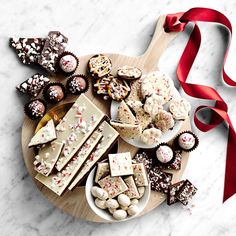 a wooden platter filled with assorted chocolates and candies next to a red ribbon