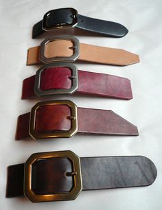 five different belts are lined up on a white table top, one is gold and the other has brown leather