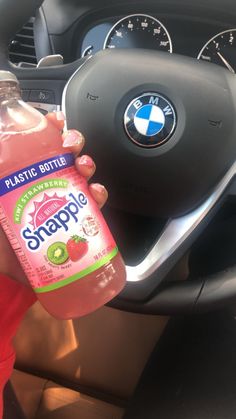 a person holding a bottle of drink in their hand next to a car steering wheel