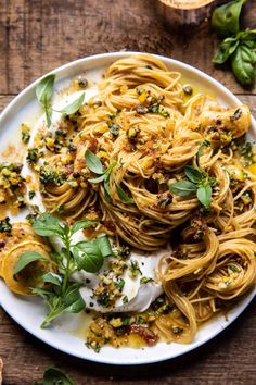 a white plate filled with pasta and sauce on top of a wooden table next to bread