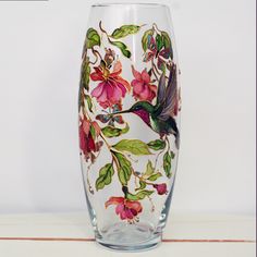 a glass vase with flowers and birds painted on the side, sitting on a table