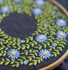 a close up of a blue and green flower embroidered on a black cloth with wooden hoop