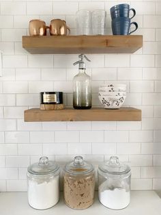 three shelves above the kitchen counter with jars and containers on them, one shelf holding two mugs