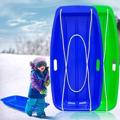 a young child standing in the snow next to two large blue and green coolers