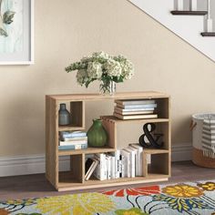 a book shelf with flowers and books on it in front of a stair case next to a rug