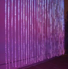 purple lights hanging from the ceiling in front of a wall that has beads attached to it