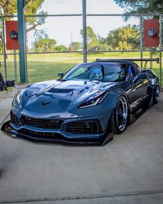 a blue sports car parked in front of a fenced in area with trees and grass