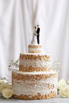 a wedding cake with white frosting and two people on top, surrounded by flowers